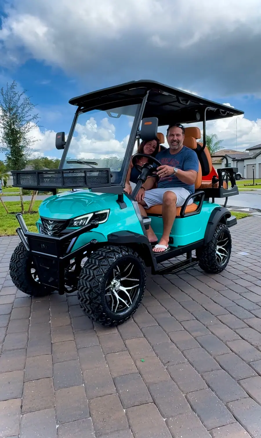 Customers seated in their new teal six-seater golf cart on a paver driveway